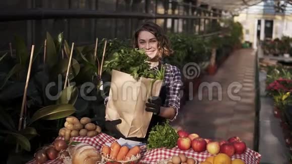 穿着围裙的年轻白种人围裙手里拿着棕色纸袋里面放着新鲜蔬菜和蔬菜一边笑着摆姿势视频的预览图