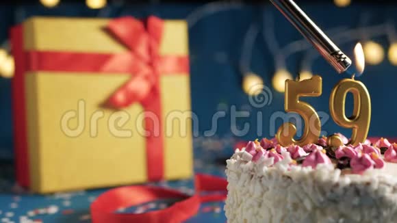 白色生日蛋糕数字59金蜡烛用打火机燃烧蓝色背景灯和礼品黄色盒子用红色系起来视频的预览图