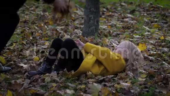 小可爱的女孩躺在美丽的公园里的秋日草地上而她的妈妈在秋天扔树叶家庭乐趣视频的预览图