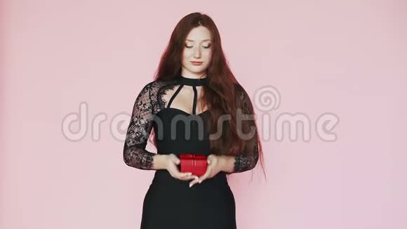 美丽的红发女孩穿着黑色连衣裙拿出一份礼物给相机笑容喜庆的心情主题是3月8日慢动作视频的预览图