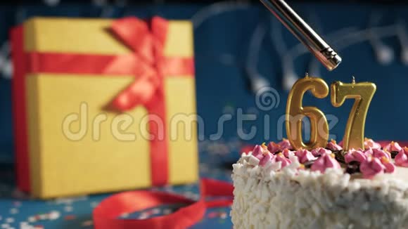 白色生日蛋糕数字67金蜡烛由打火机燃烧蓝色背景灯和礼品黄色盒子与红色捆绑视频的预览图