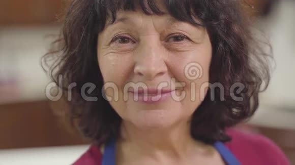 一个微笑的高加索族妇女的特写脸棕色的眼睛和卷曲的头发看着相机快乐退休视频的预览图