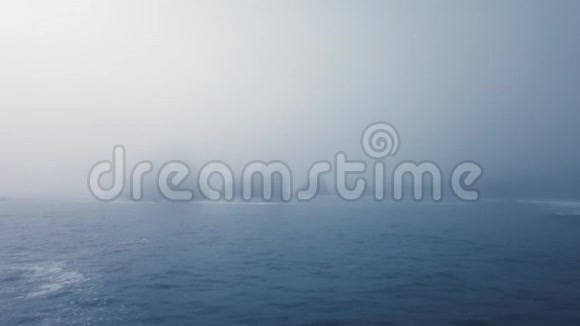 无人机摄像机在从平静的蓝色海洋中突出出来的浓雾中接近岩石视频的预览图