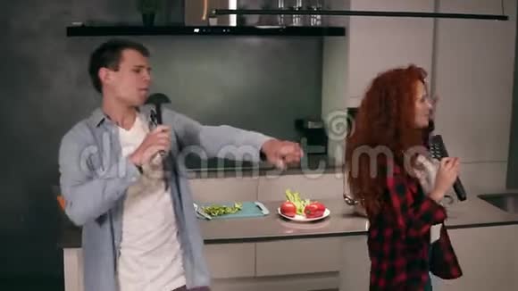 白种人年轻的家庭夫妇丈夫和红头发的妻子一起用汤勺和通心粉麦克风唱歌视频的预览图