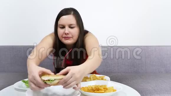 厚厚的可爱女孩坐在沙发上吃快餐汉堡包薯片视频的预览图