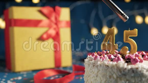 白色生日蛋糕编号45金色蜡烛用打火机燃烧蓝色背景灯和礼品黄色盒子系好视频的预览图