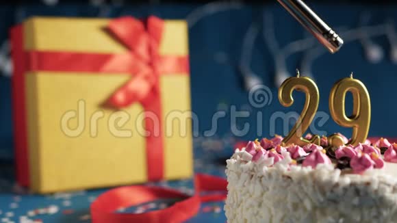 白色生日蛋糕29号金色蜡烛点燃打火机蓝色背景灯和礼品黄盒捆绑在一起视频的预览图