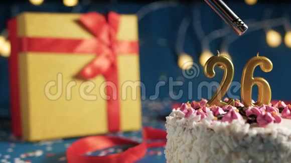 白色生日蛋糕26号金色蜡烛由打火机点燃蓝色背景灯和礼品黄色盒子绑在一起视频的预览图