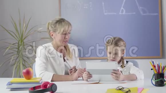 镜头慢慢地接近白人妇女和女学生坐在桌子上与平板电脑中学导师教学视频的预览图