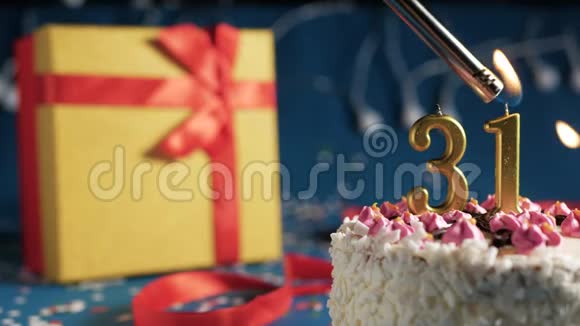 白色生日蛋糕31号金色蜡烛由打火机点燃蓝色背景灯和礼品黄色盒子捆绑视频的预览图