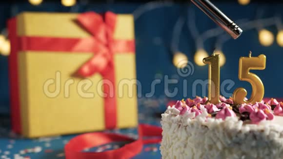 白色生日蛋糕数字15金蜡烛点燃打火机蓝色背景灯和礼品黄盒子捆绑视频的预览图