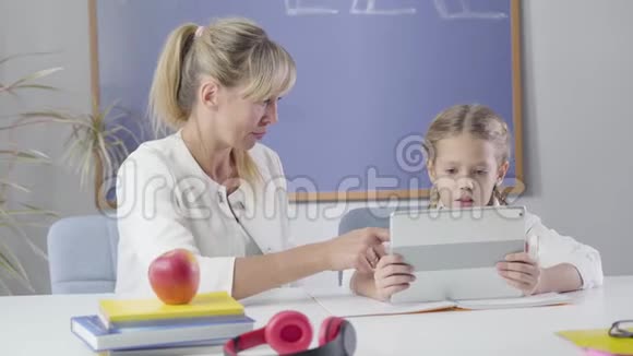 一幅白种人成年女性和小女学生坐在桌子旁的平板电脑的肖像智能导师教学视频的预览图