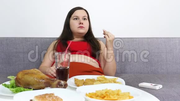 丰满的女人坐在桌子旁吃高热量的垃圾食品看电视视频的预览图