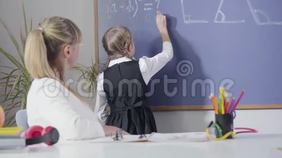 白人小女孩在黑板上写数学公式坐在餐桌前的中年教师视频的预览图