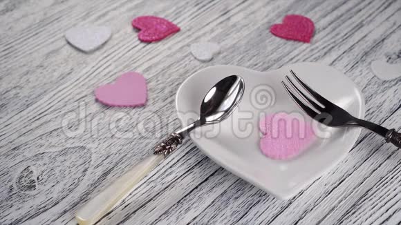 装饰的心落在心形盘子上上面有甜点叉子和勺子在木质轻盈质感的桌子上粉红色和白色视频的预览图