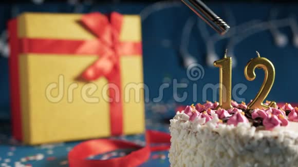 白色生日蛋糕12号金烛由打火机点燃蓝色背景与灯和礼品黄色盒子捆绑视频的预览图