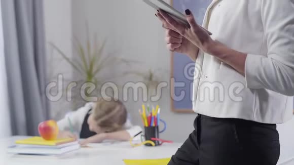 成年白种人妇女站在平板电脑上像一个小漂亮的女学生在练习本上写作孩子学习模糊视频的预览图