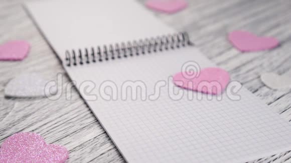 闪闪发光的纸心落在一个打开的笔记本上黑色的金属捆绑在白色的木制纹理桌子上视频的预览图