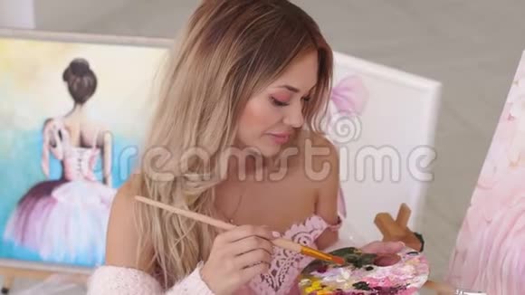 穿着粉红色针织毛衣的女孩在画室的帆布上画花视频的预览图