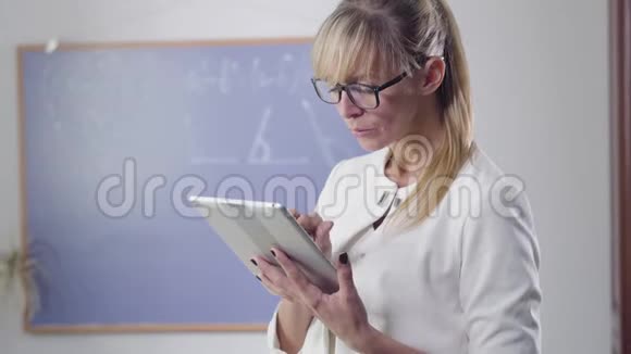 集中的中年白种人妇女站在平板电脑和回首优雅眼镜的私人教师视频的预览图