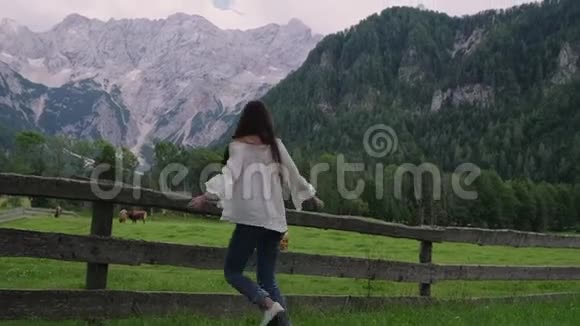 年轻女子在阿尔卑斯山和农场附近的草地上跳跃和旋转视频的预览图