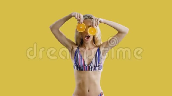 年轻漂亮的女孩正在跳舞微笑着手里拿着黄色背景的橘子快乐健康瘦女人视频的预览图