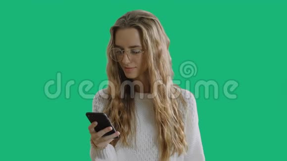 戴着时髦眼镜的漂亮年轻女人拿着智能手机用智能手机在绿色屏幕上微笑视频的预览图