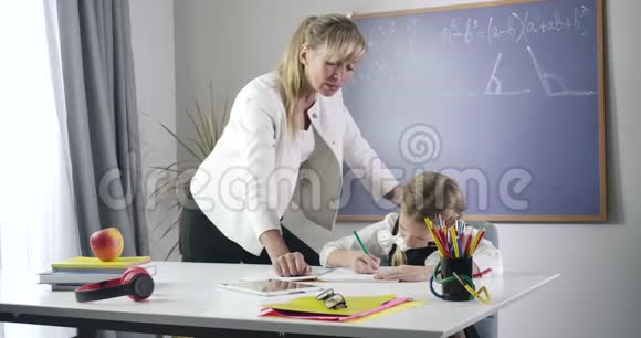 中年白种人家庭教师站在女学生旁边写作业本私人教师和勤奋的孩子视频的预览图