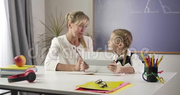 中年白种人妇女和小女生坐在桌旁拿着平板电脑和学习数学教育视频的预览图
