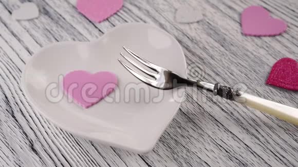 装饰的心落在带有甜点叉子的心形盘子上在木质轻盈的纹理桌子上视频的预览图