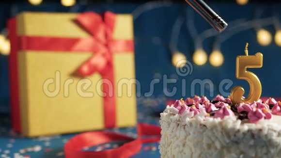 白色生日蛋糕5号金烛由打火机点燃蓝色背景与灯和礼品黄色盒子捆绑视频的预览图