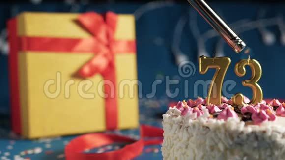 白色生日蛋糕编号73金色蜡烛由打火机燃烧蓝色背景灯和礼品黄色盒子与红色捆绑视频的预览图