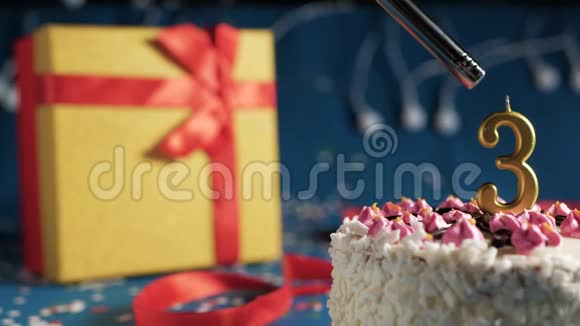 白色生日蛋糕3号金烛由打火机点燃蓝色背景与灯和礼品黄色盒子捆绑视频的预览图