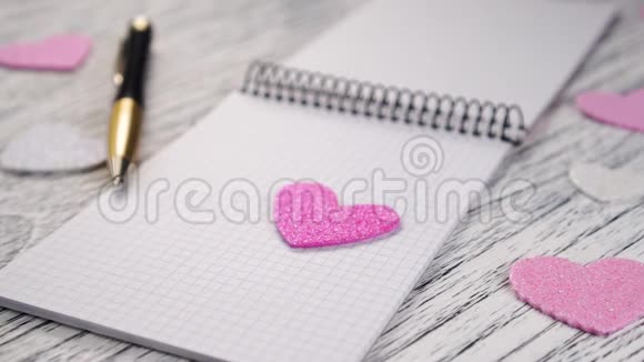 粉红色和白色的细纸心落在黑色金属装订的笔记本上视频的预览图