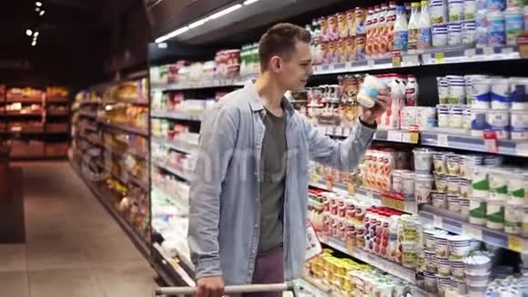 微笑着时尚的男人在大商场里带着购物车走在货架旁拿着牛奶产品突然视频的预览图