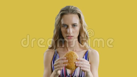年轻瘦瘦的漂亮女人正在吃黄色或橙色背景的汉堡包瘦女孩饿了视频的预览图