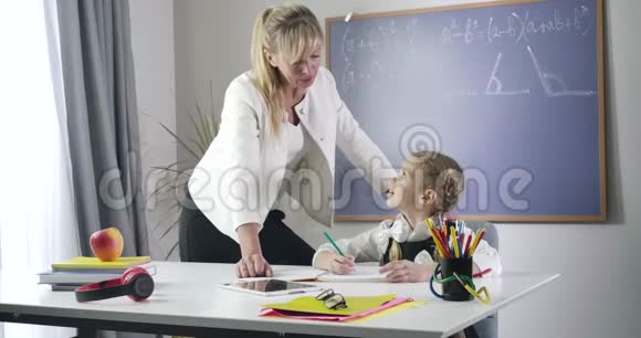 自信的白种人中年家庭教师穿着正式西装站在女学生旁边看着她练习写作视频的预览图