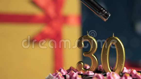 生日蛋糕30支金色蜡烛用打火机点燃蓝色背景礼品黄色盒子用红丝带系好视频的预览图