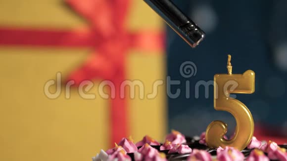 生日蛋糕5号金色蜡烛用打火机燃烧蓝色背景礼品黄色盒子用红色丝带绑起来关闭视频的预览图