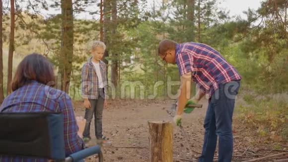 父亲一起在夏林的露营地砍柴爸爸和儿子在家庭露营时用斧头砍木头视频的预览图