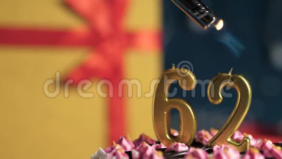 生日蛋糕62号金色蜡烛用打火机点燃蓝色背景礼品黄色盒子用红丝带系好视频的预览图