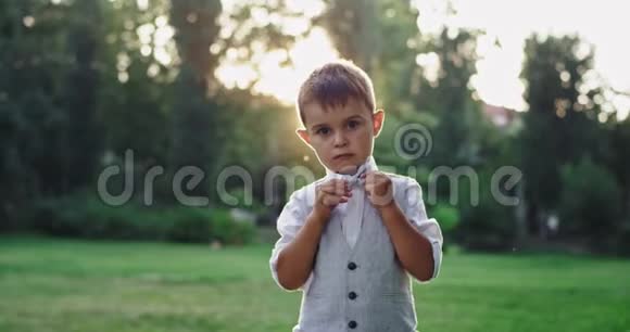 镜头前可爱的5岁男孩在公园中央严肃的脸上打着蝴蝶结视频的预览图