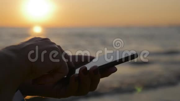 女人的手在海滩上使用手机背景是美丽的日落海滩度假概念视频的预览图