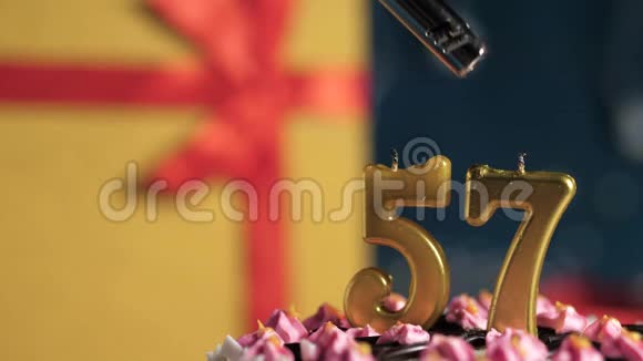 生日蛋糕编号57的金色蜡烛用打火机点燃蓝色背景礼品黄色盒子用红丝带好视频的预览图