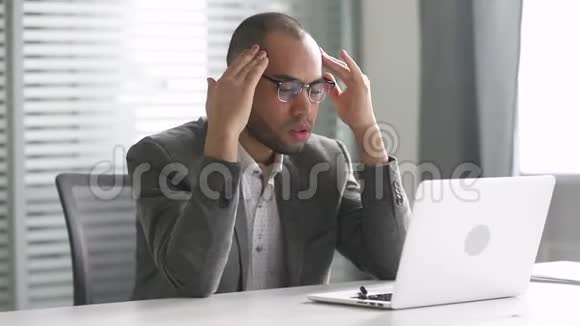 穿着衣服的非洲商人看着笔记本电脑感到头疼视频的预览图