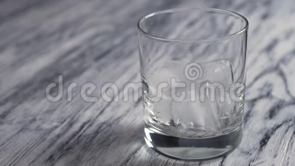 金色威士忌倒入一个装有冰块的玻璃杯中放在一个老式的木制灰色柜台上视频的预览图