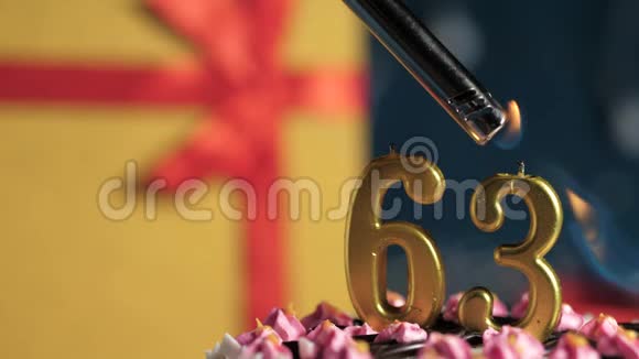 生日蛋糕编号63金色蜡烛用打火机点燃蓝色背景礼品黄色盒子用红丝带系好视频的预览图
