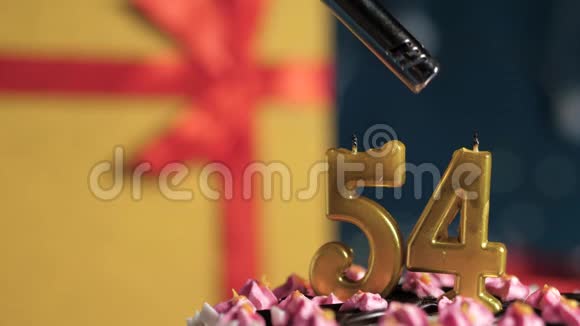 生日蛋糕54号金色蜡烛用打火机点燃蓝色背景礼品黄色盒子用红色丝带系好视频的预览图