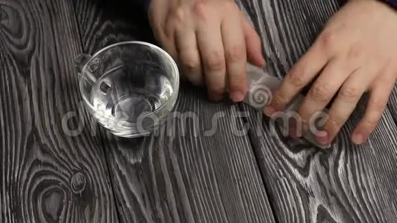 一个人从装有药丸的药盒中取出一颗药丸他另一只手拿着一杯水在一张桌子的背景下视频的预览图