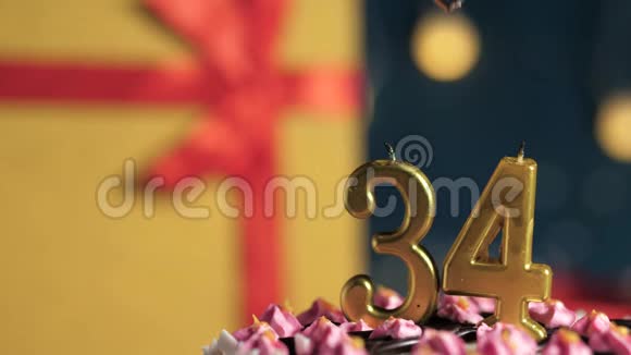 生日蛋糕编号34金色蜡烛用打火机点燃蓝色背景礼品黄色盒子用红丝带系好视频的预览图